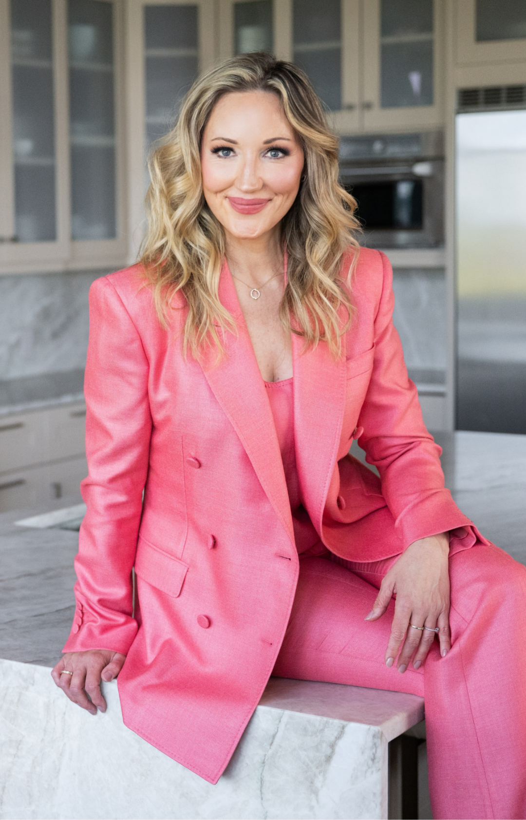debbie in pink suit smiling and sitting on countertop